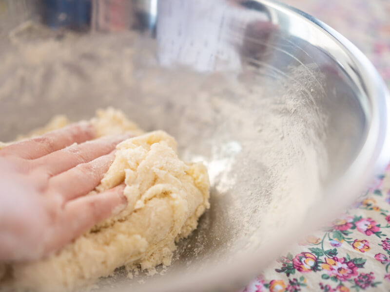 A hand rolls some fresh gnocchi dough in a floured metal bowl